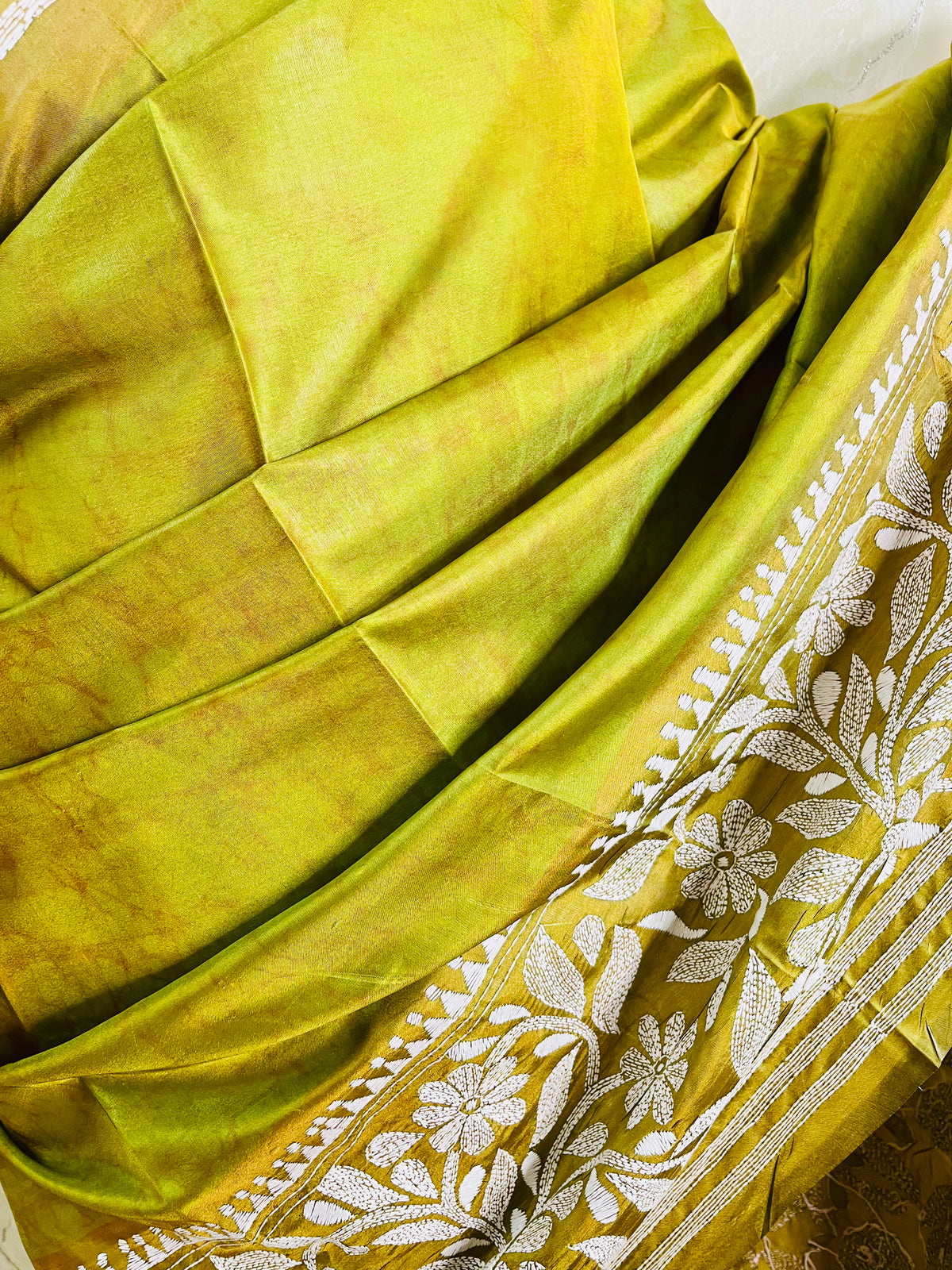 Close-up of the handcrafted white Katha stitch floral motifs and subtle batik dye texture on the olive green blended Bangalore silk saree