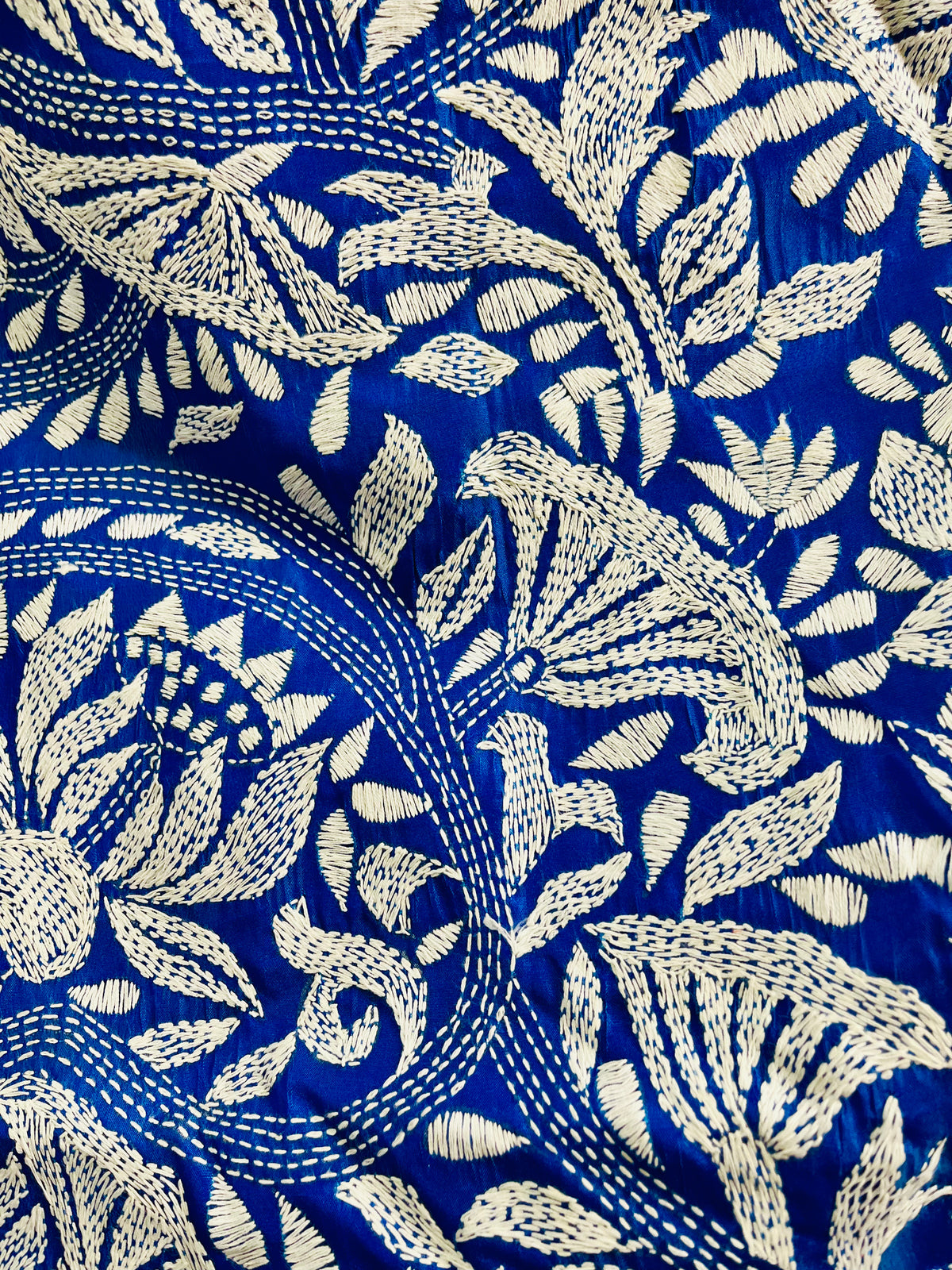 Close-up of white Kantha running stitch branches, leaves and seed-pod blooms on royal blue silk