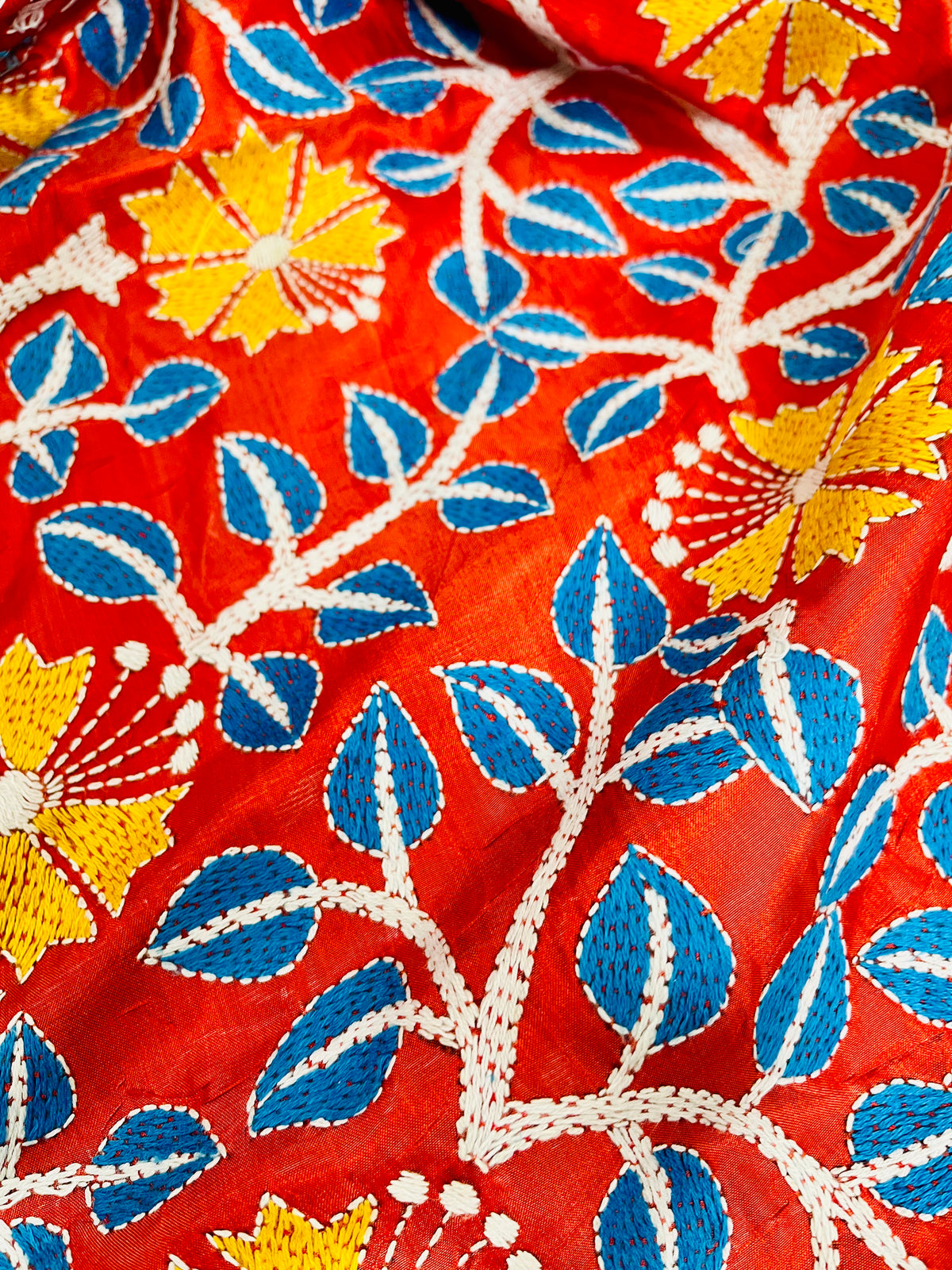 Detail of white and sky blue Kutch work cross-stitch lattice beside Kantha leaf motifs on vermilion silk