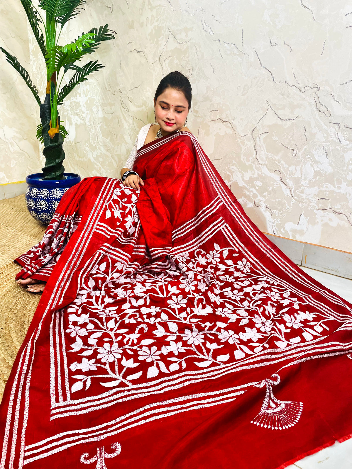 Seated pose in crimson red batik Kantha stitch saree with white flower and leaf pallu on Bangalore silk