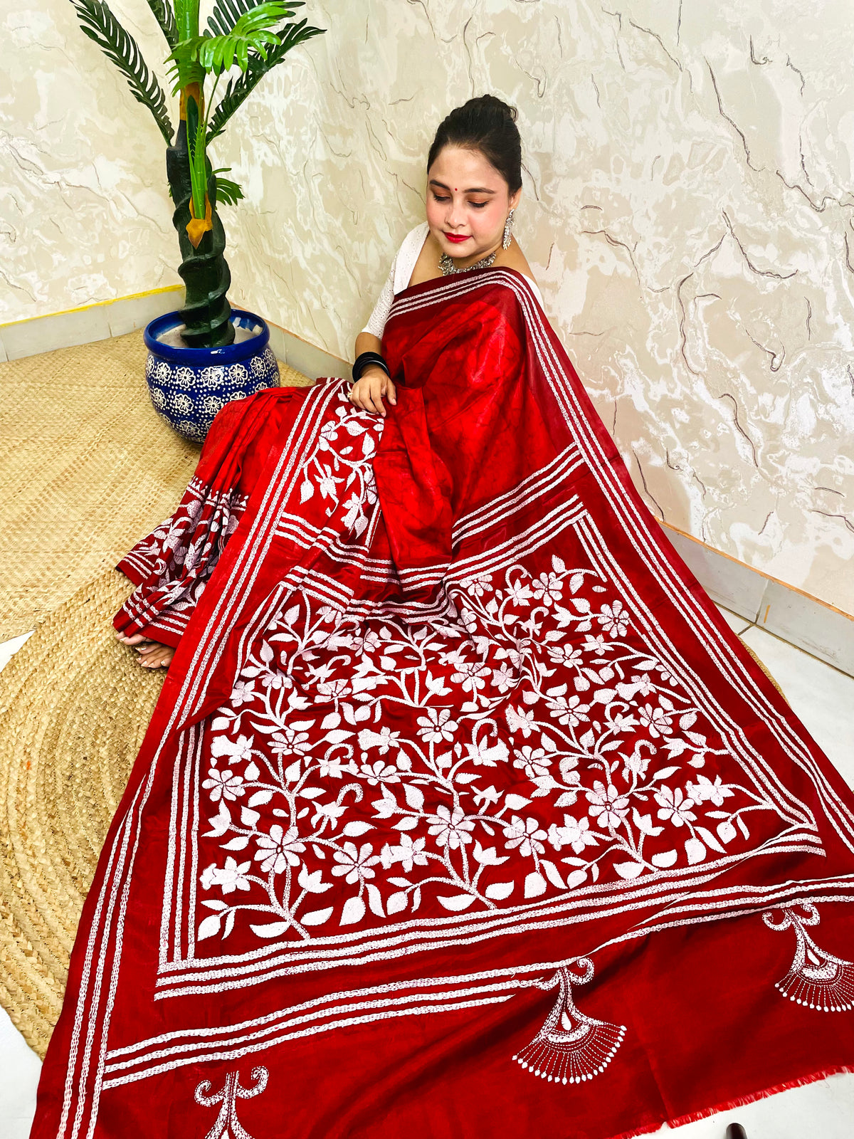 Top view of seated drape in crimson red batik saree with white Kantha floral panel and striped bands