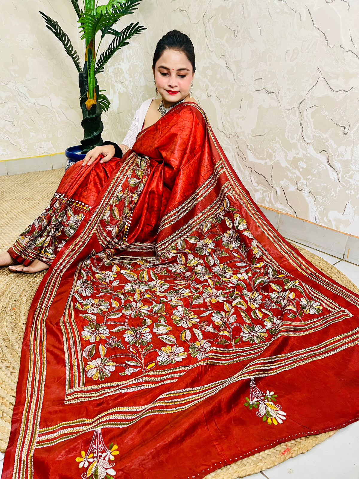 Seated pose in rust red batik Kantha saree with striped border and floral pallu