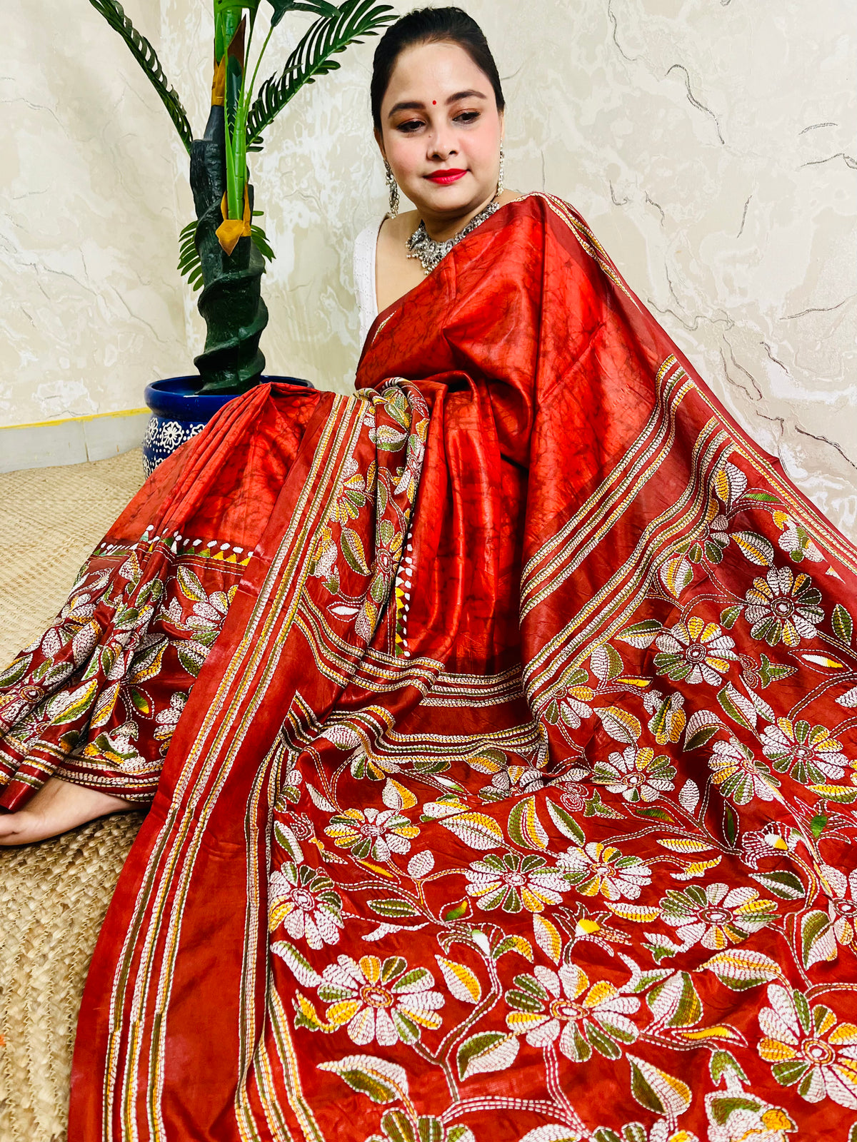 Seated drape of rust red Kantha stitch saree showing hanging floral motif at pallu end