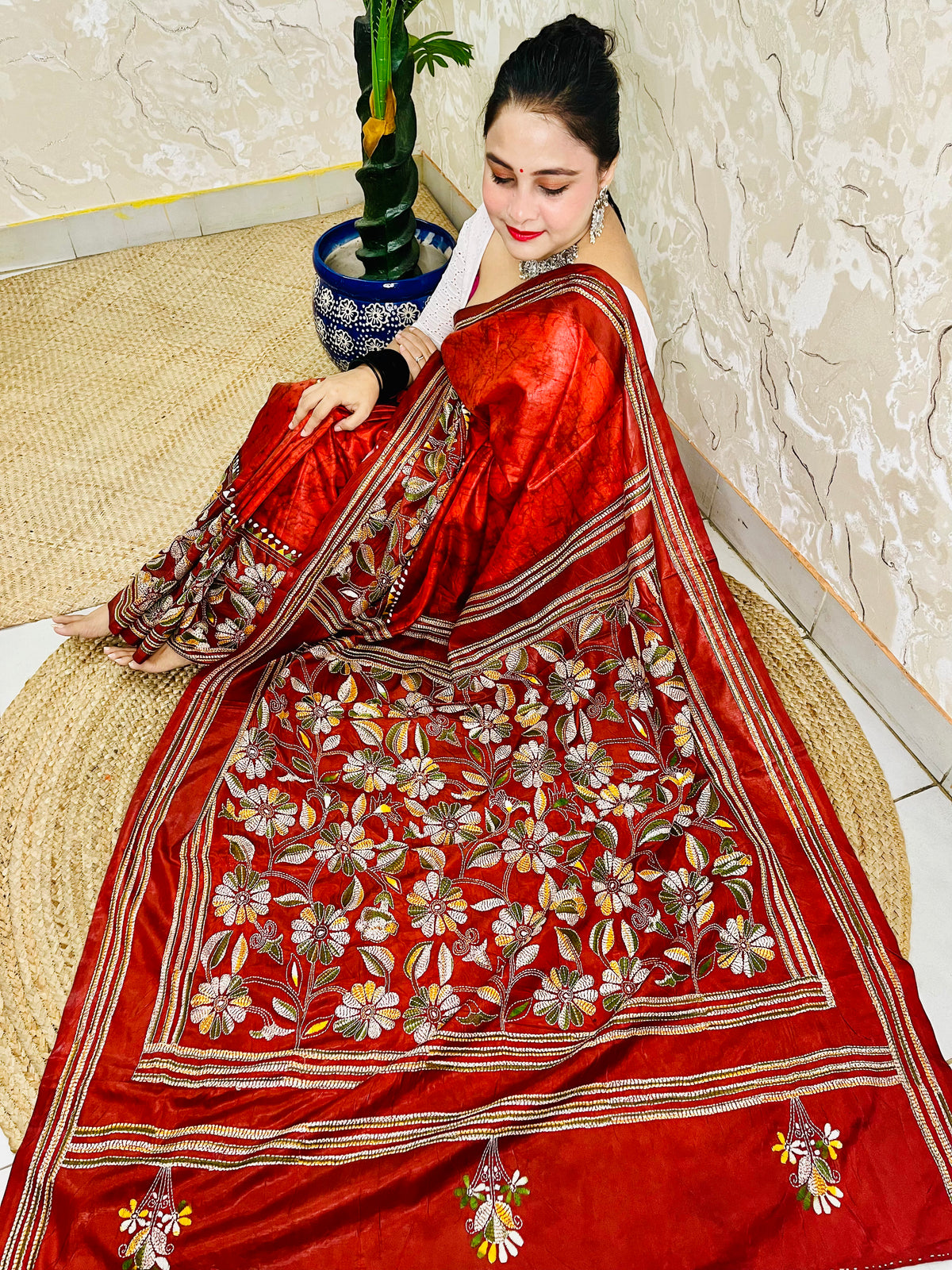Seated pose in rust red batik Kantha saree with striped border and floral pallu