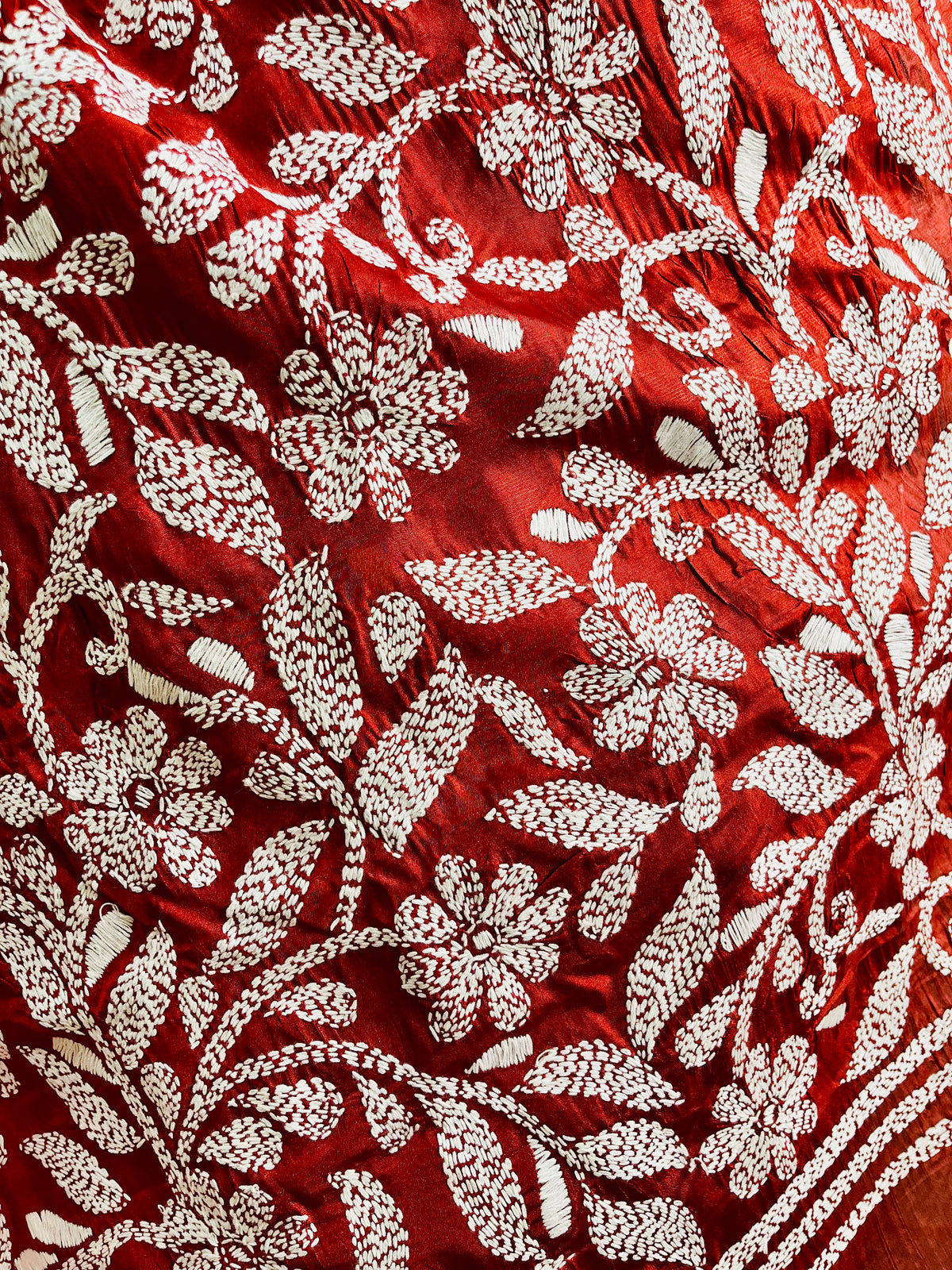 Close-up of crimson batik silk with white Kantha stitch floral embroidery