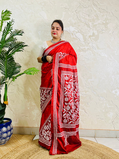 Woman holding crimson batik saree pallu showing dense floral Kantha work