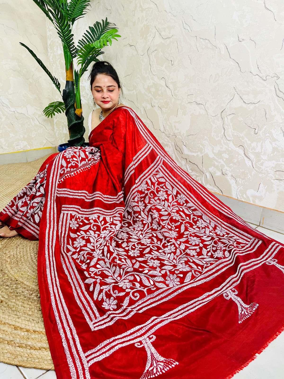 Seated pose in red batik Kantha saree with tree motif pallu on silk