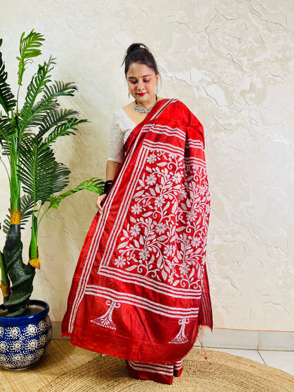 Woman holding crimson batik saree pallu showing dense floral Kantha work