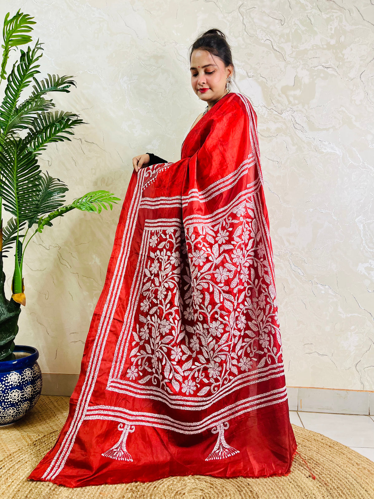 Woman holding crimson batik saree pallu showing dense floral Kantha work