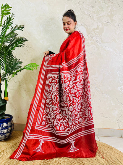 Woman holding crimson batik saree pallu showing dense floral Kantha work