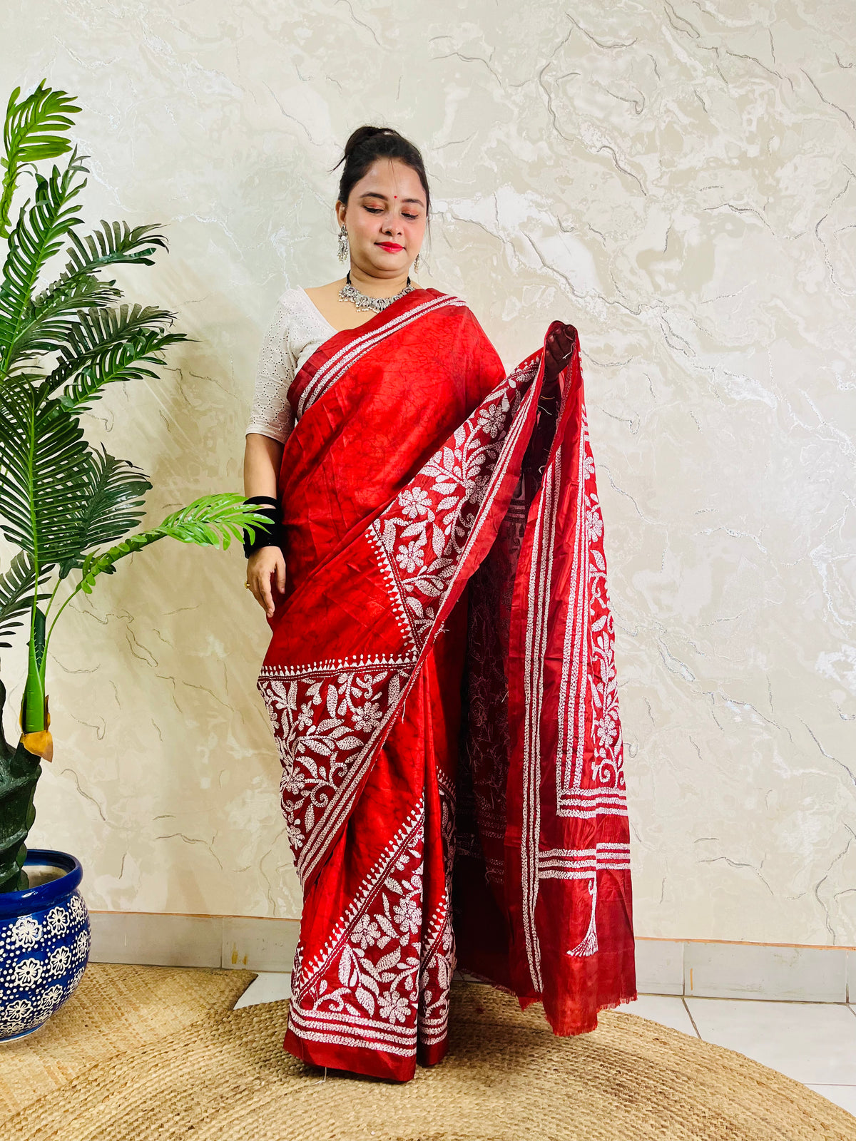 Woman holding crimson batik saree pallu showing dense floral Kantha work