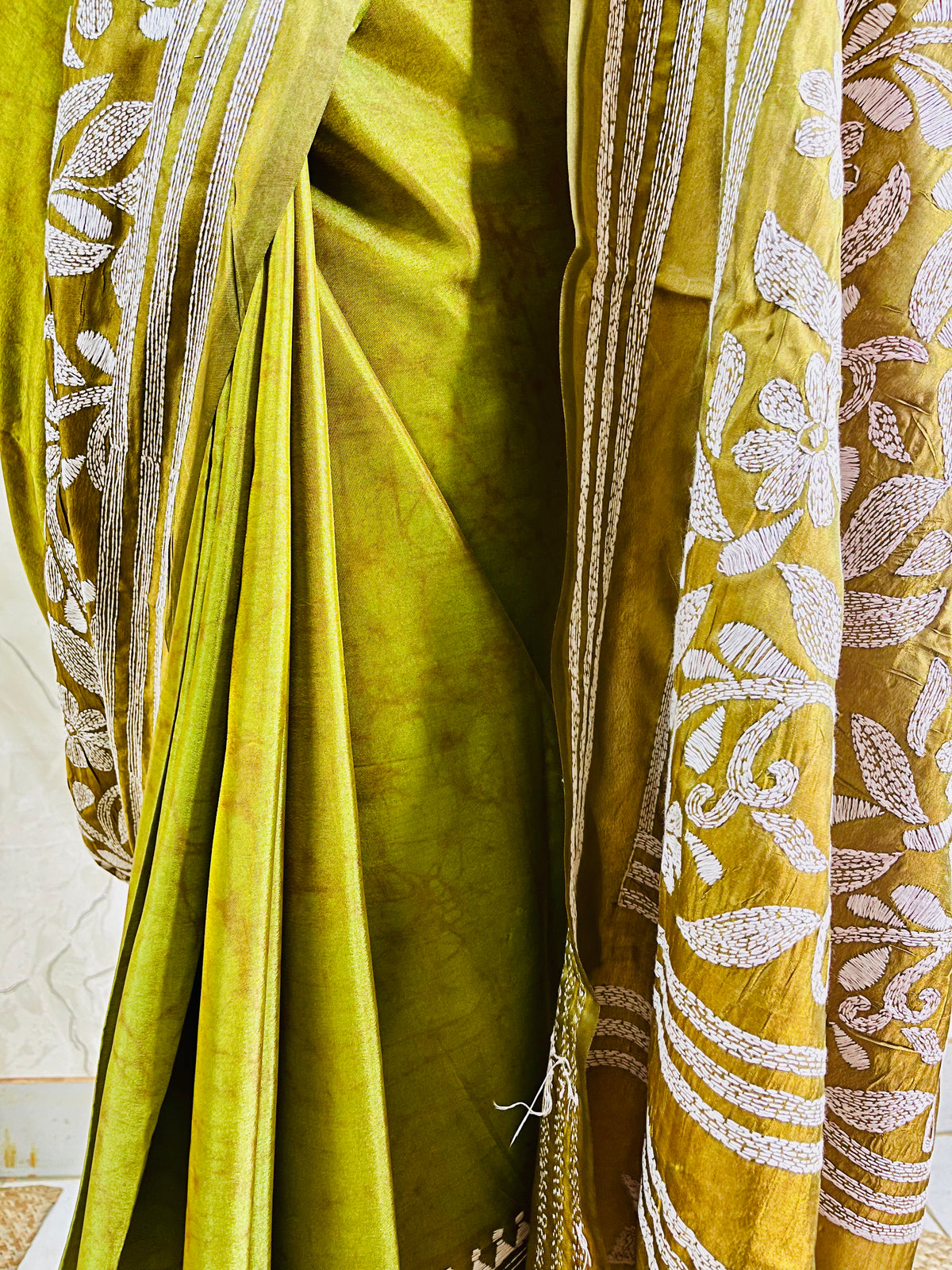 Close-up of the handcrafted white Katha stitch floral motifs and subtle batik dye texture on the olive green blended Bangalore silk saree