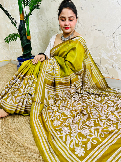 Woman sitting elegantly showcasing the dense, handcrafted white floral Katha embroidery on the pallu of the olive green Batik saree