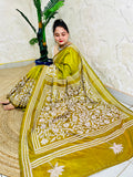 Woman sitting elegantly showcasing the dense, handcrafted white floral Katha embroidery on the pallu of the olive green Batik saree