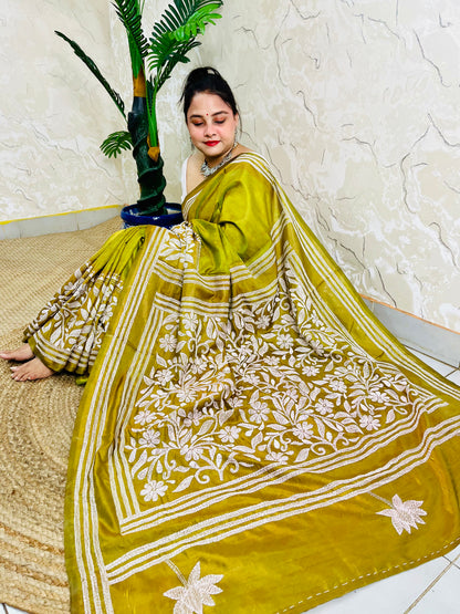 Woman sitting elegantly showcasing the dense, handcrafted white floral Katha embroidery on the pallu of the olive green Batik saree