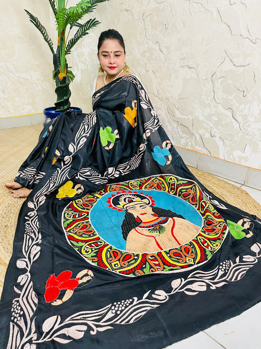 Front seated view of black Kantha saree with colourful face portrait and cream vine border
