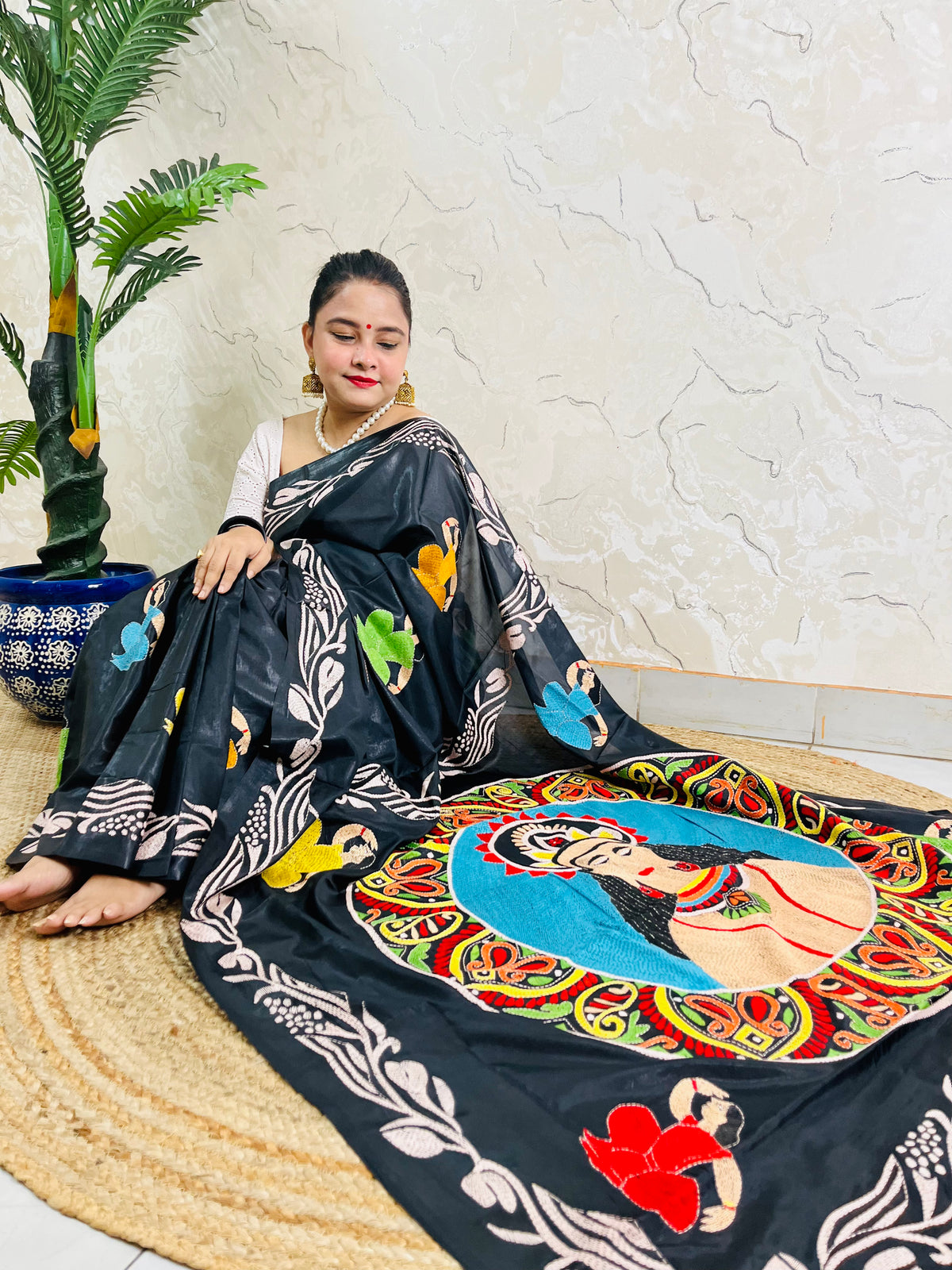 Front seated view of black Kantha saree with colourful face portrait and cream vine border