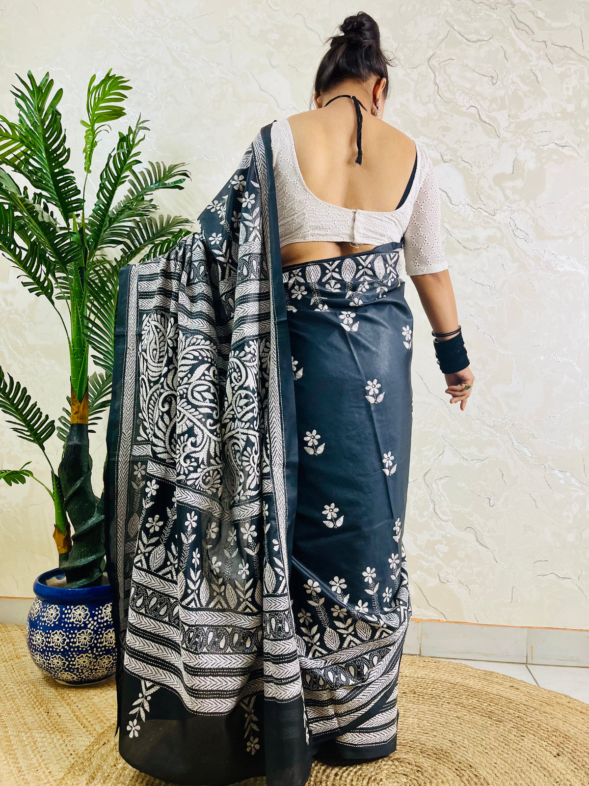 Back view of a woman draped in the black Katha stitch silk saree highlighting the grand, heavily embroidered paisley pallu