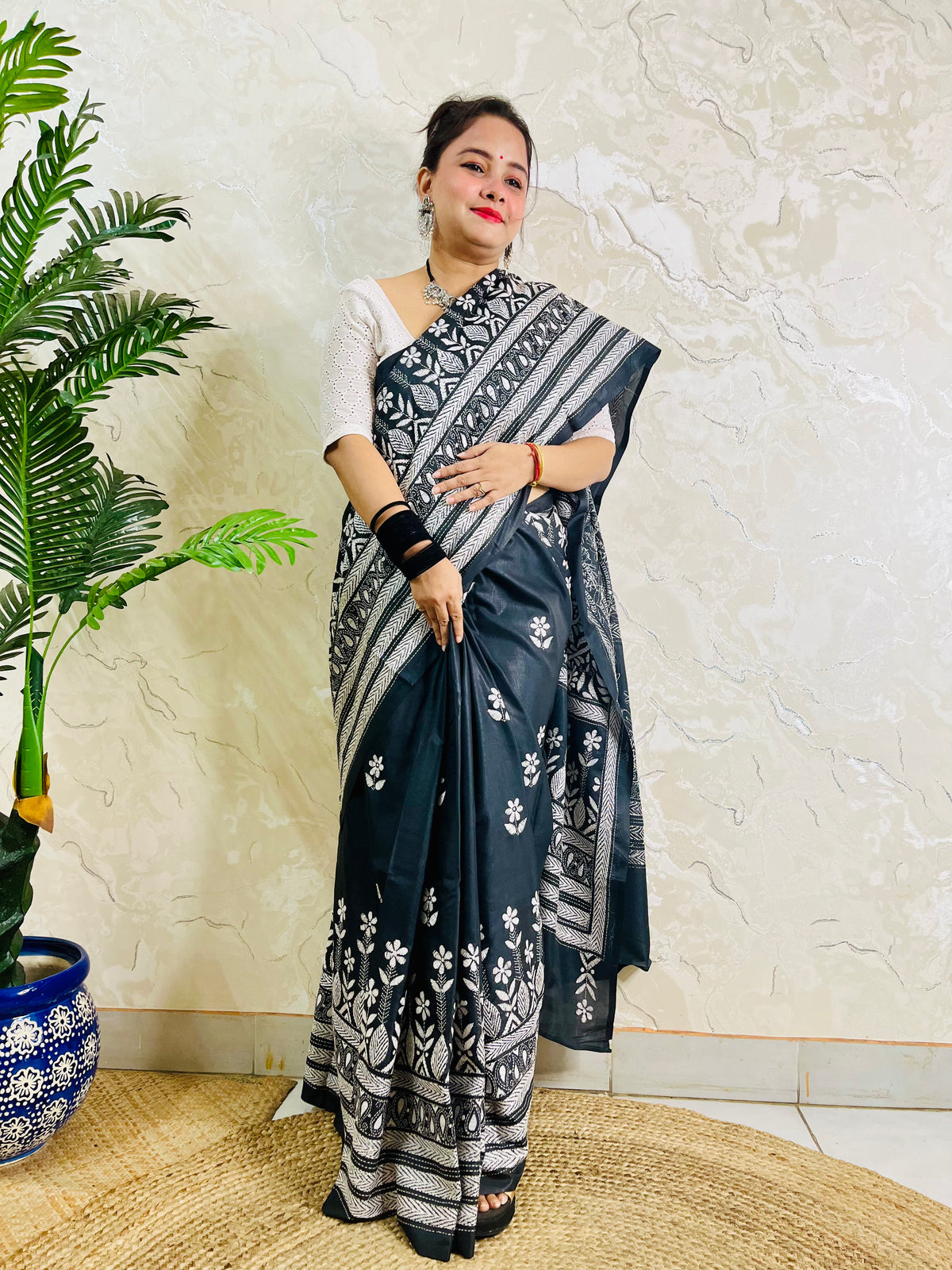 Woman standing with the black handcrafted saree draped to show the scattered floral bootis on the body and elaborate border work