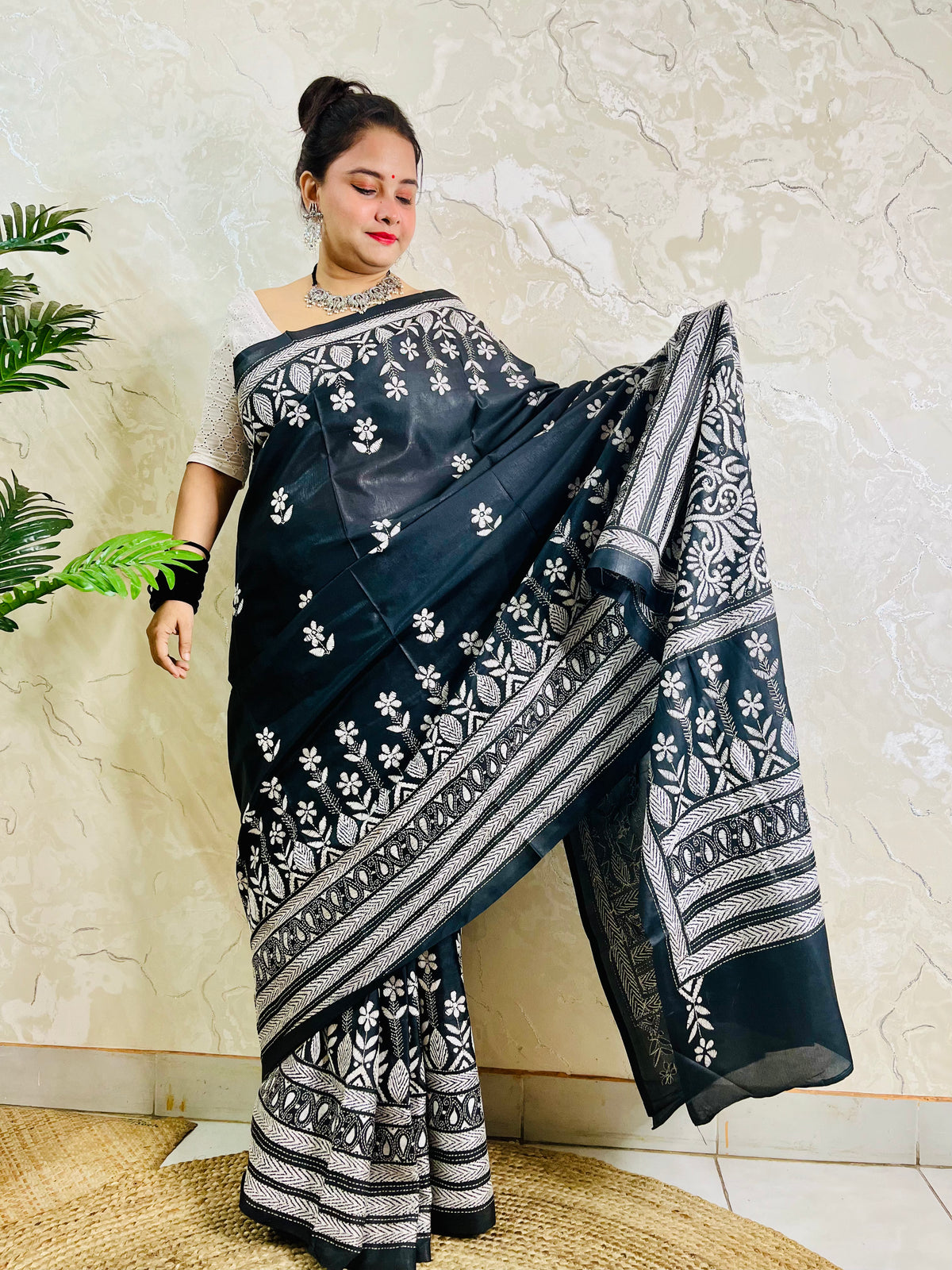 Woman standing with the black handcrafted saree draped to show the scattered floral bootis on the body and elaborate border work
