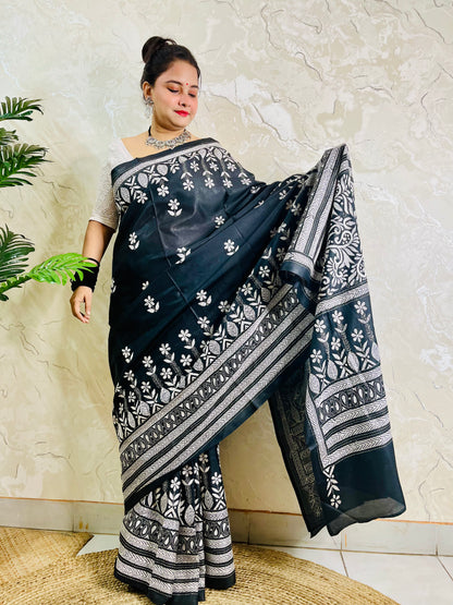 Woman standing with the black handcrafted saree draped to show the scattered floral bootis on the body and elaborate border work