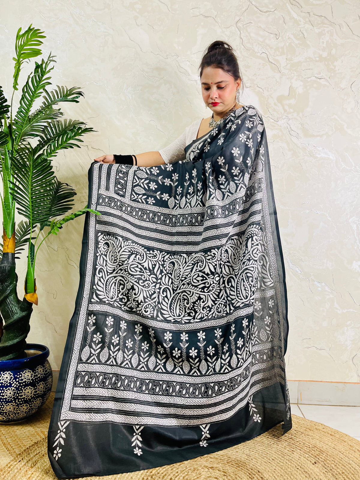 Woman standing with the black handcrafted saree draped to show the scattered floral bootis on the body and elaborate border work