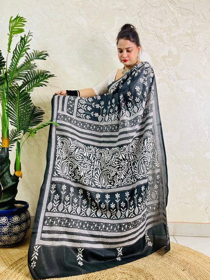 Woman standing with the black handcrafted saree draped to show the scattered floral bootis on the body and elaborate border work
