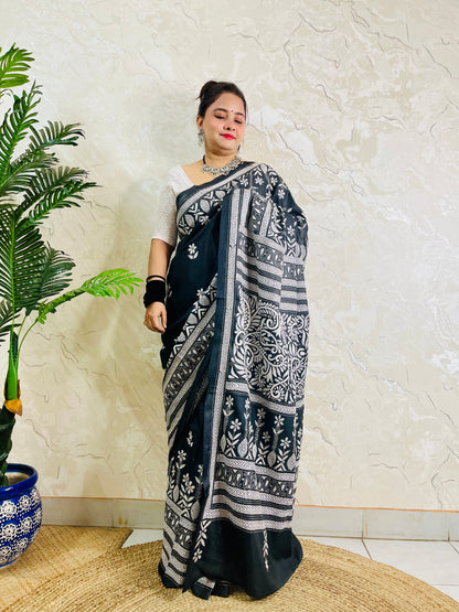 Woman standing with the black handcrafted saree draped to show the scattered floral bootis on the body and elaborate border work