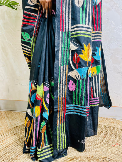 Woman holding open pallu of black Kantha saree showing striped lotus border