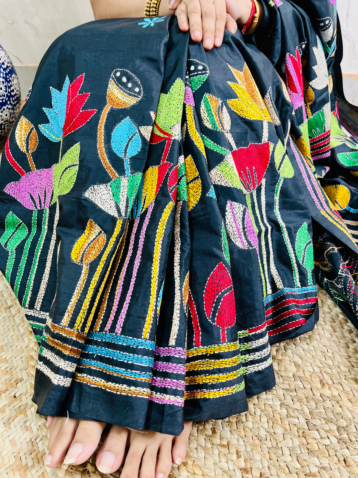 Woman holding open pallu of black Kantha saree showing striped lotus border