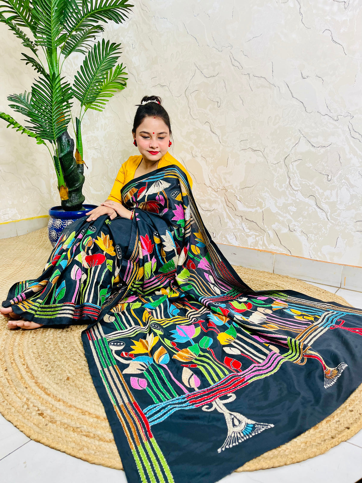 Woman seated in black multicolour Kantha stitch saree, front pallu spread view