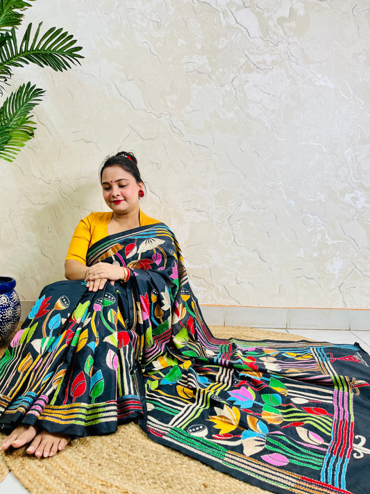Woman seated in black multicolour Kantha stitch saree, front pallu spread view