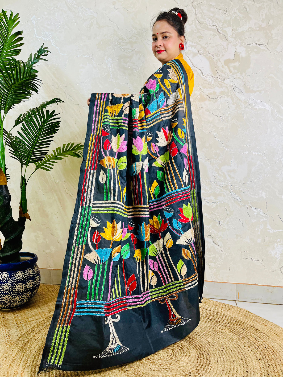 Woman holding open pallu of black Kantha saree showing striped lotus border