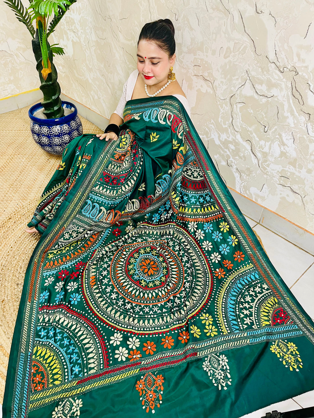 High-angle sitting pose displaying the spread-out hand-embroidered Mandala artwork and vibrant geometric thread work on deep bottle green silk.