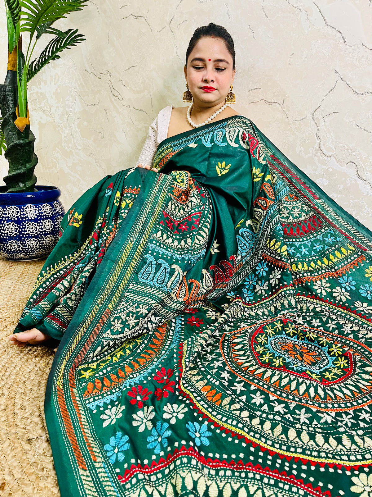 High-angle sitting pose displaying the spread-out hand-embroidered Mandala artwork and vibrant geometric thread work on deep bottle green silk.