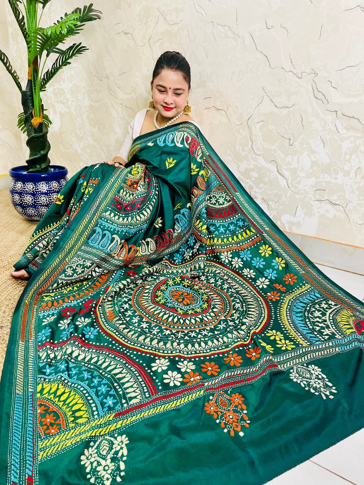 High-angle sitting pose displaying the spread-out hand-embroidered Mandala artwork and vibrant geometric thread work on deep bottle green silk.