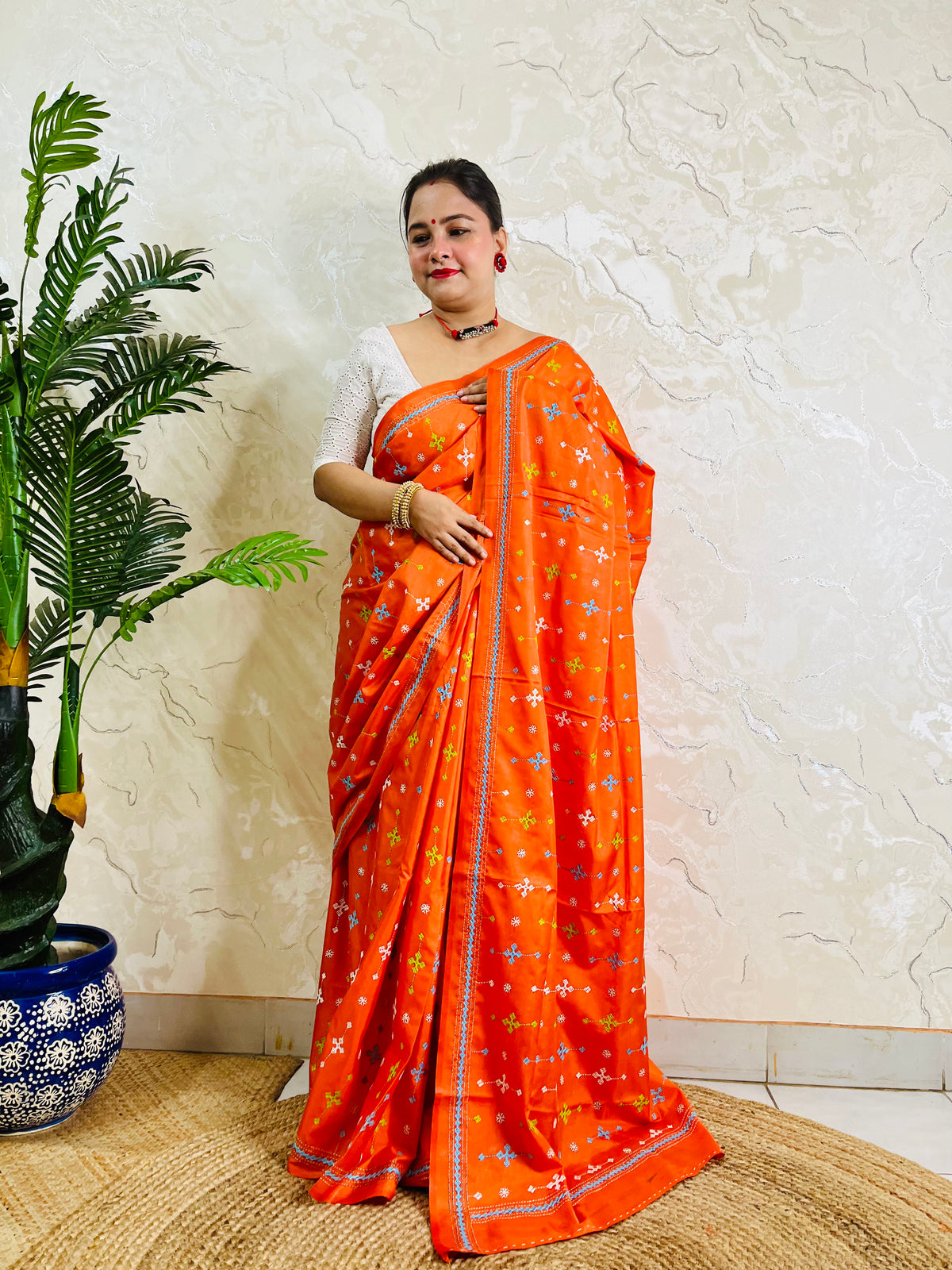 Front standing pose in bright orange saree with sky blue Kutch embroidery border