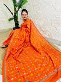 Woman seated in orange saree with blue and green cross-stitch embroidery detail