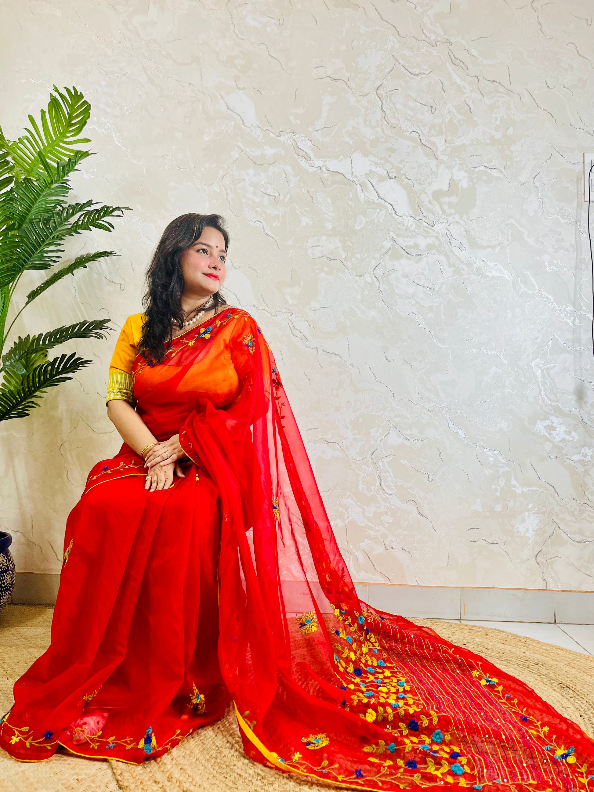 Handcrafted red organza silk saree with multicolour bullion stitch floral embroidery draped on model, side sitting view — Desi Aadat