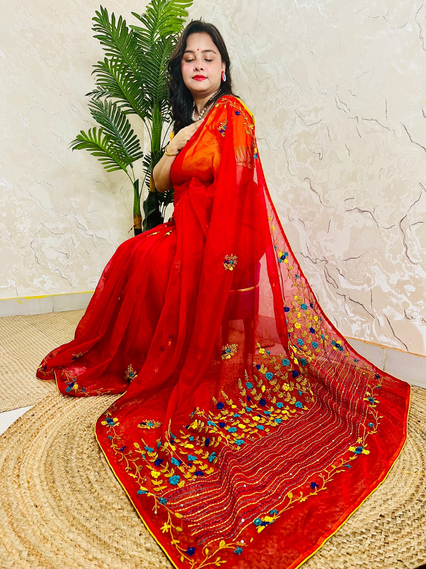 Handcrafted red organza silk saree with multicolour bullion stitch floral embroidery draped on model, side sitting view — Desi Aadat