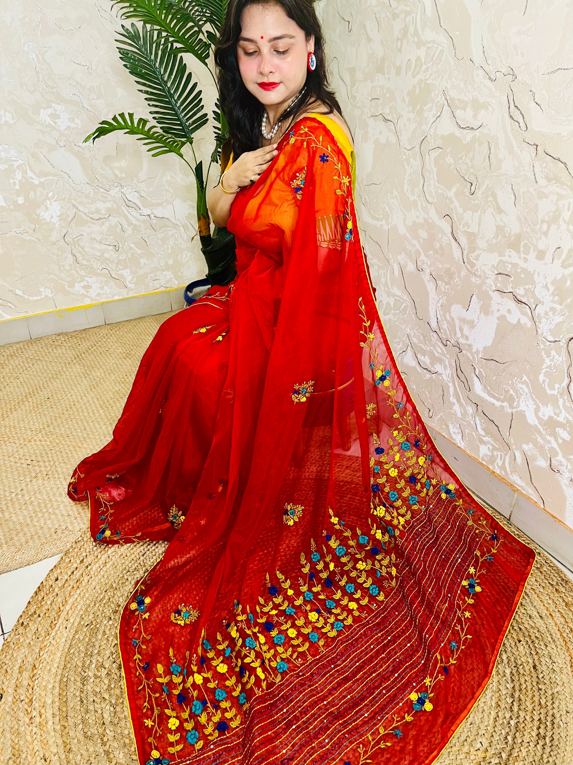 Handcrafted red organza silk saree with multicolour bullion stitch floral embroidery draped on model, side sitting view — Desi Aadat
