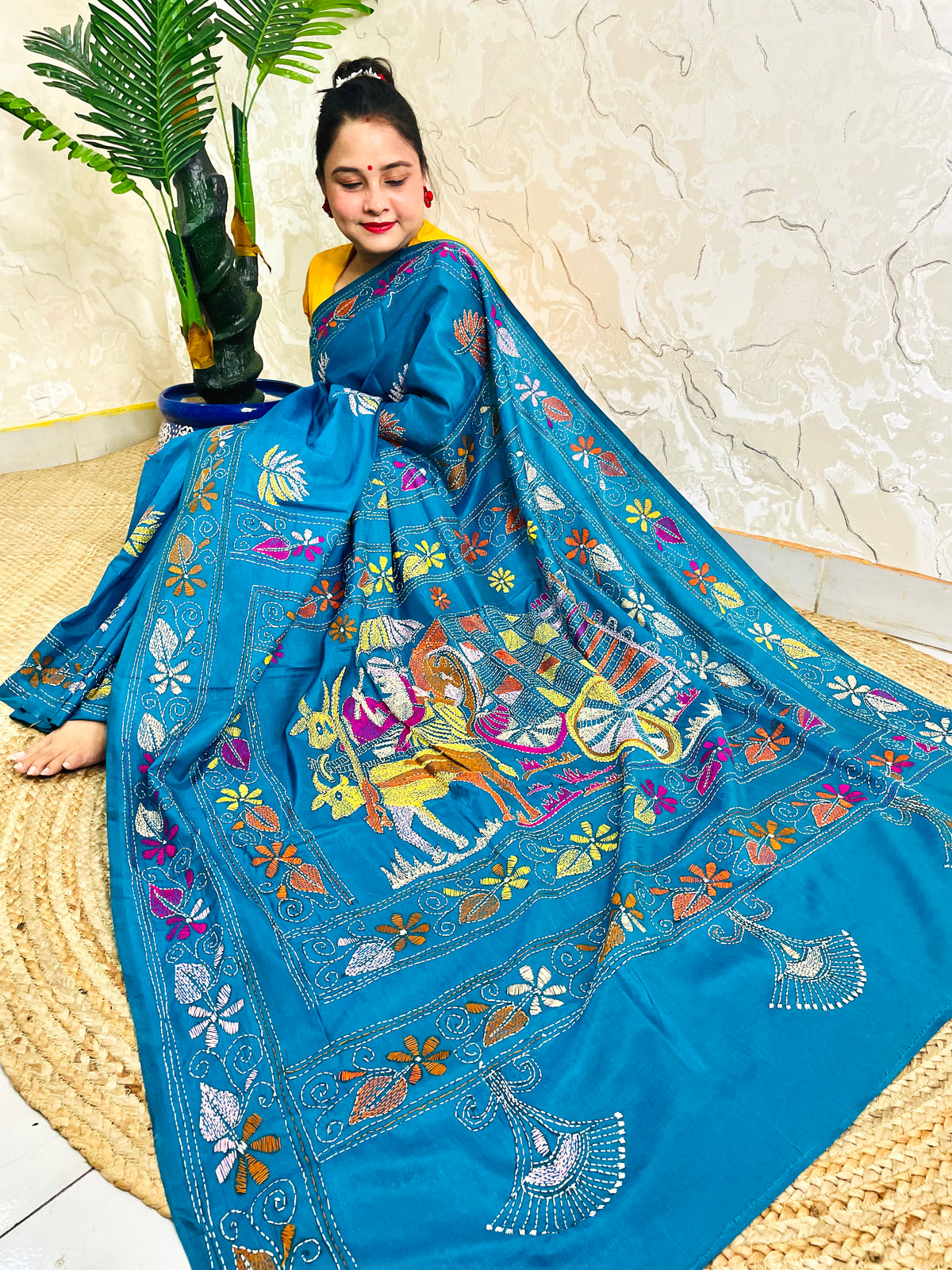 Peacock blue Kantha stitch saree with hand-embroidered bullock cart scene, seated view