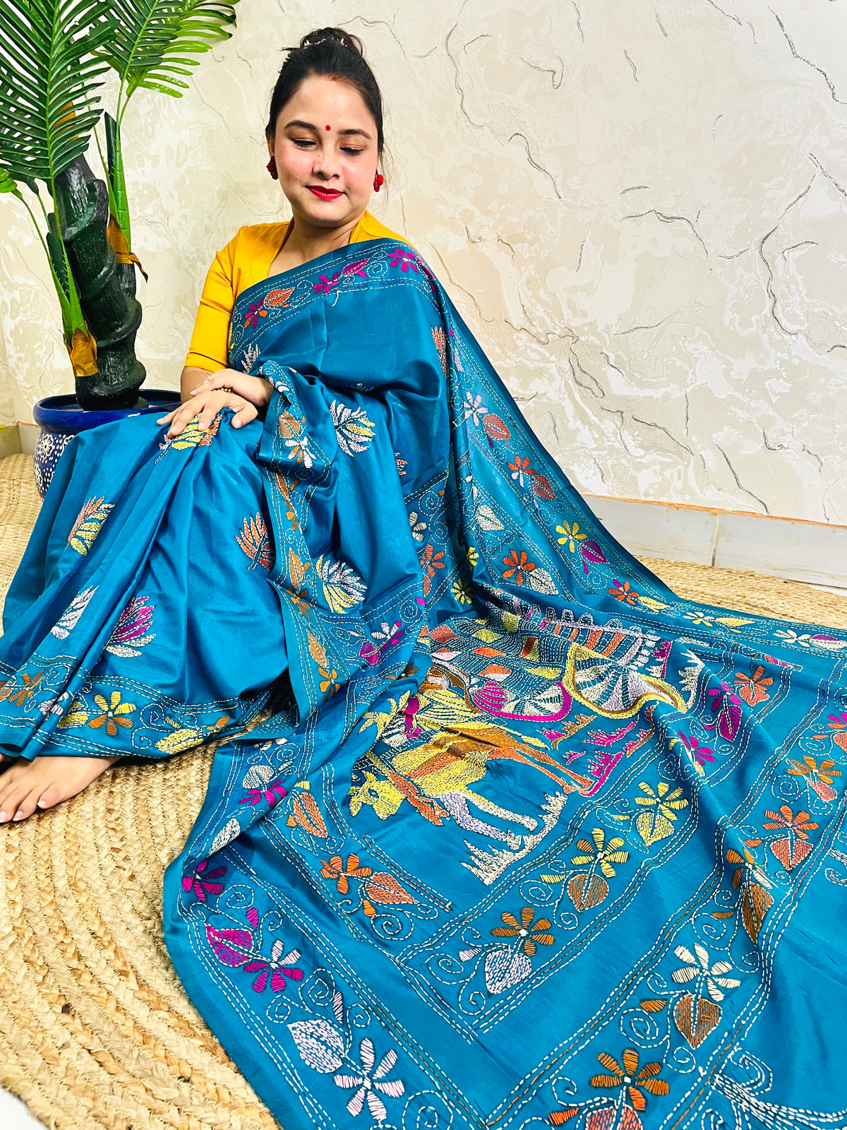 Woman seated holding open pallu showing bullock cart Kantha motif, peacock blue saree