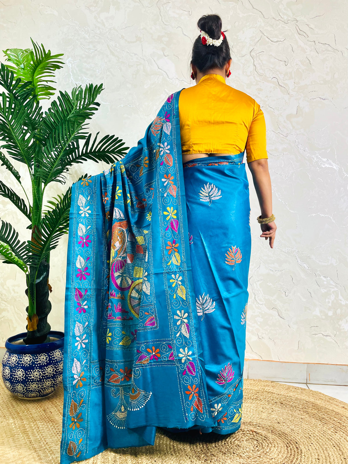 Back standing view of peacock blue Kantha stitch saree with floral border