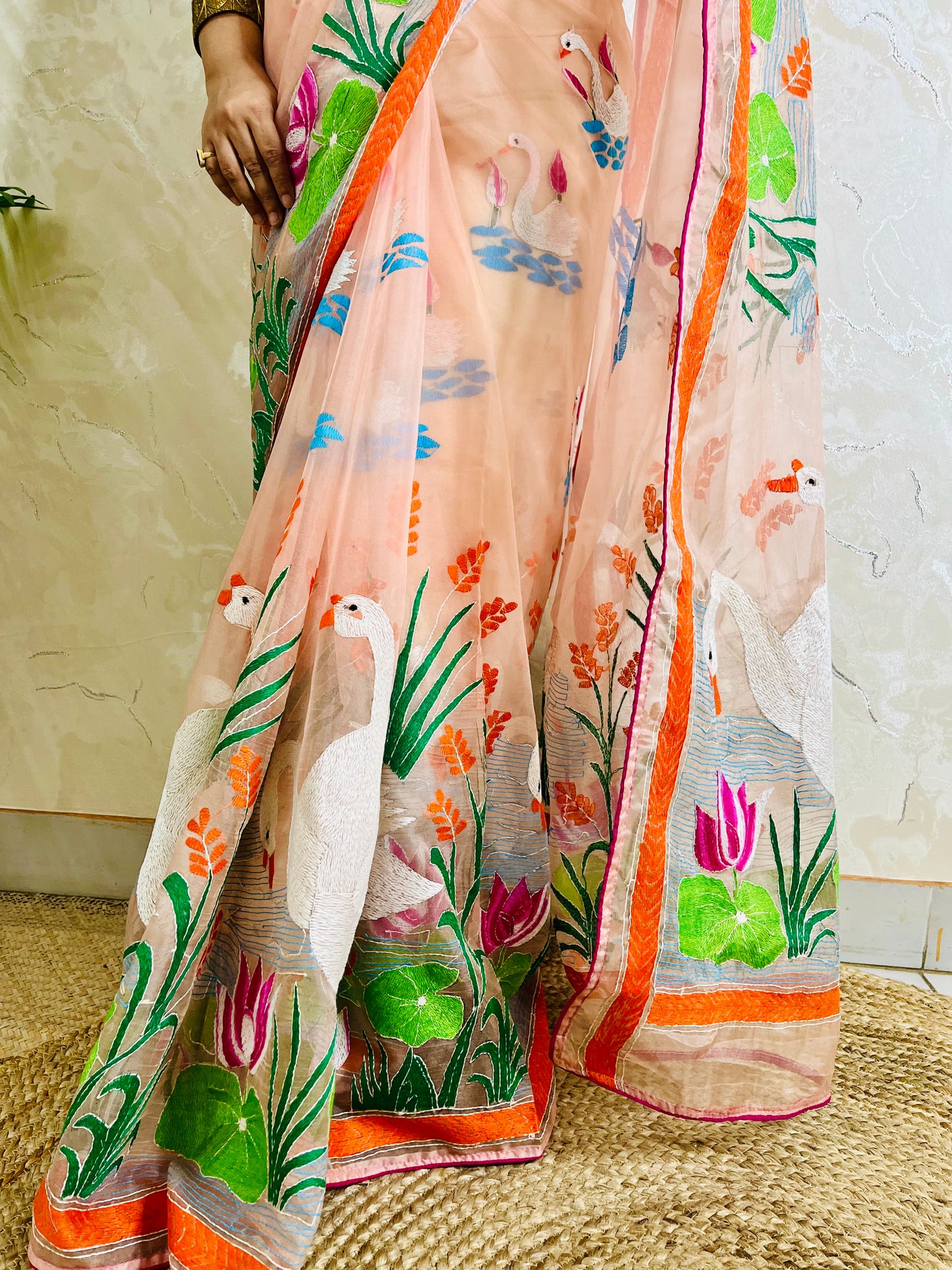 Close-up of Kantha stitch embroidery showing swans, lotus flowers and leaves on peach-pink organza saree