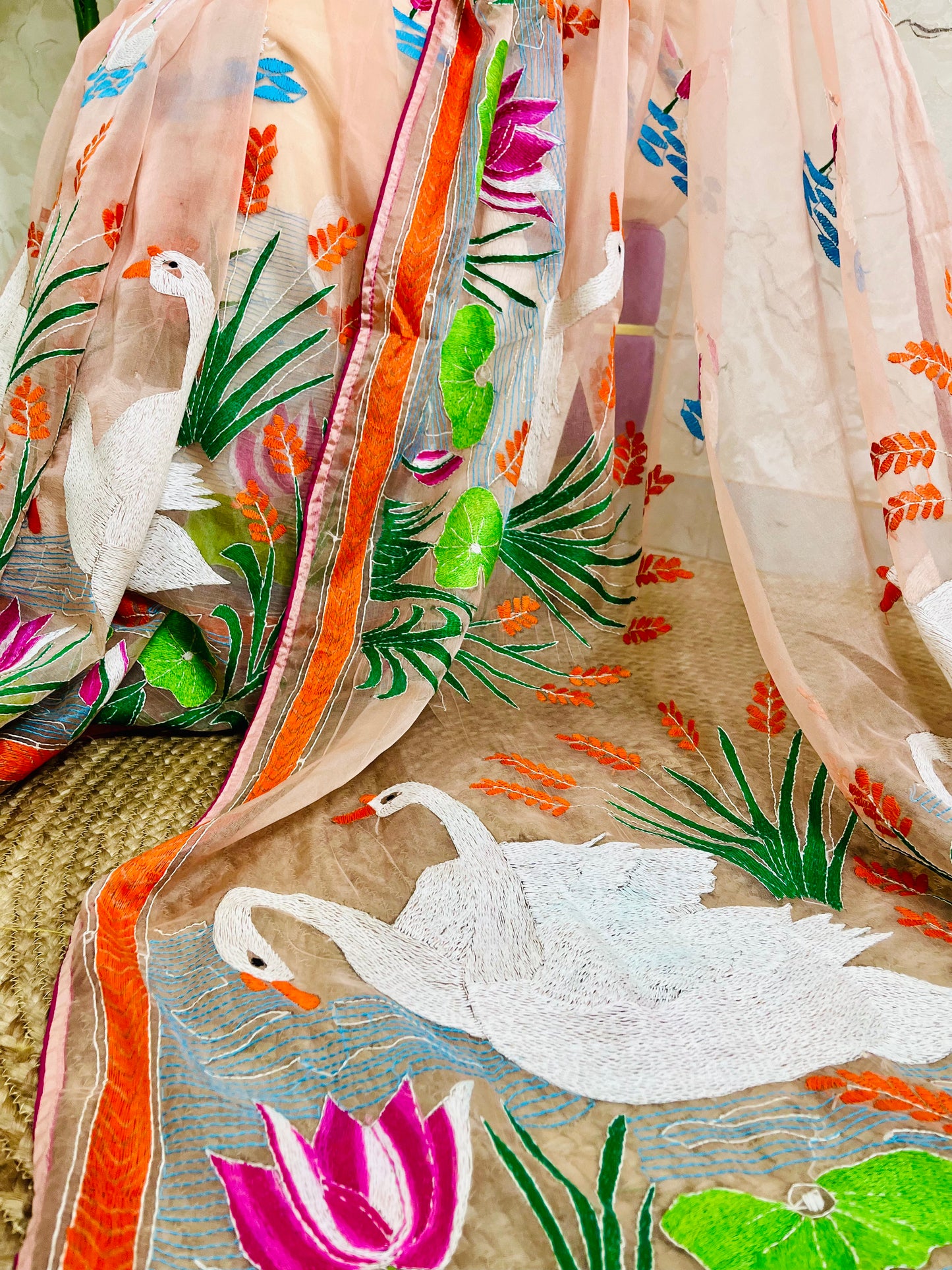 Close-up of Kantha stitch embroidery showing swans, lotus flowers and leaves on peach-pink organza saree