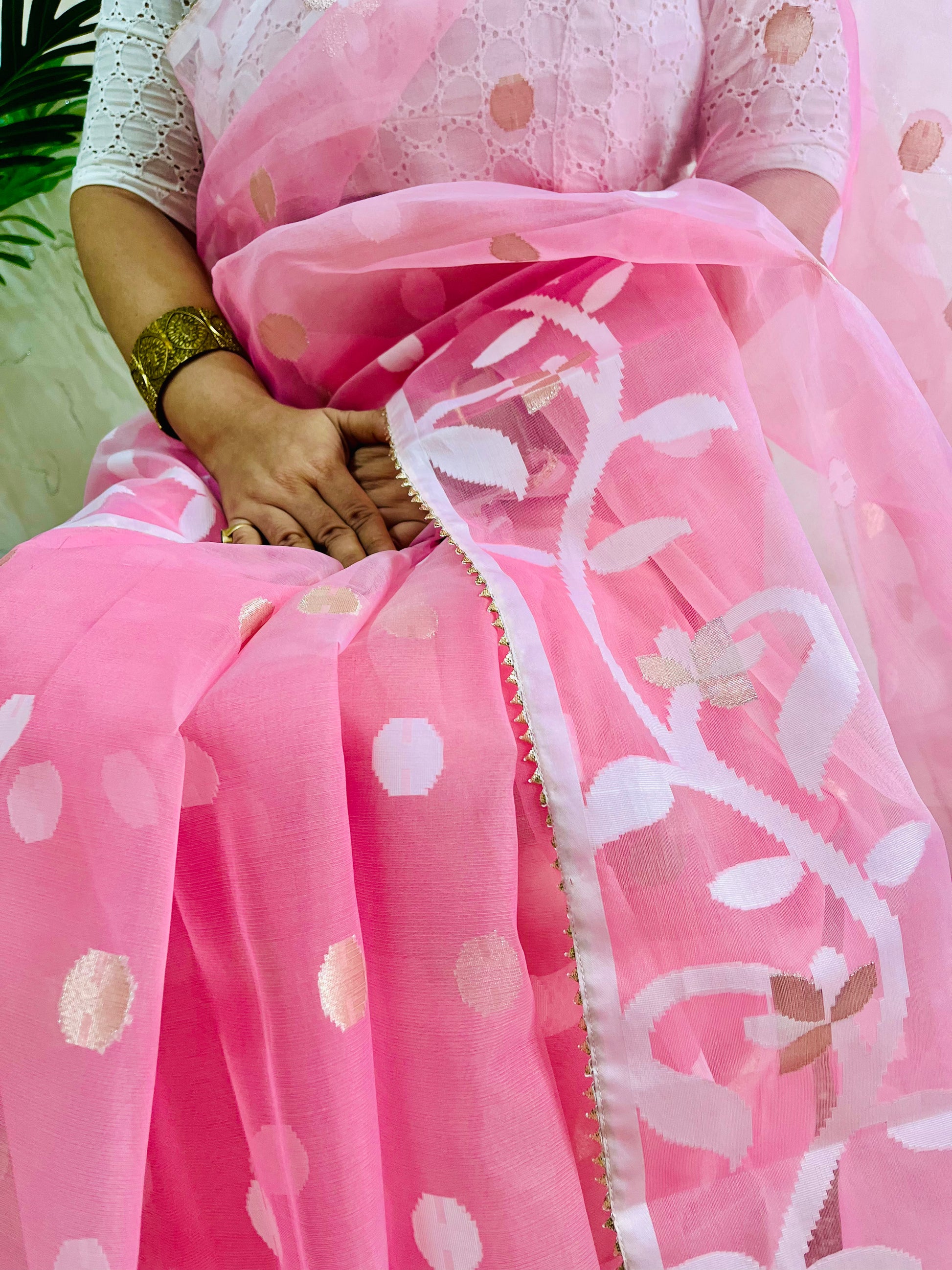 A close-up of a pink saree with white floral vine patterns and metallic gold polka dots, worn by a model with a white embroidered blouse.