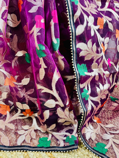 A close-up of a purple embroidered fabric, likely a saree or scarf, featuring intricate floral and leaf patterns in beige, green, orange, and pink on a sheer mesh base.