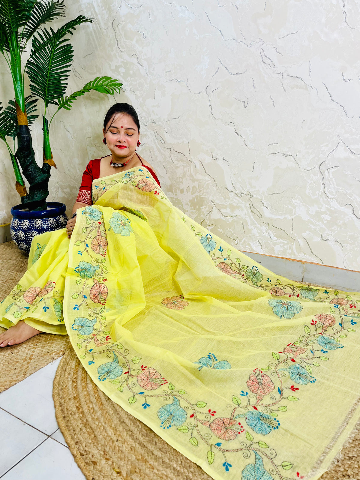Seated view of pastel yellow Tussar silk saree with hand-embroidered floral border