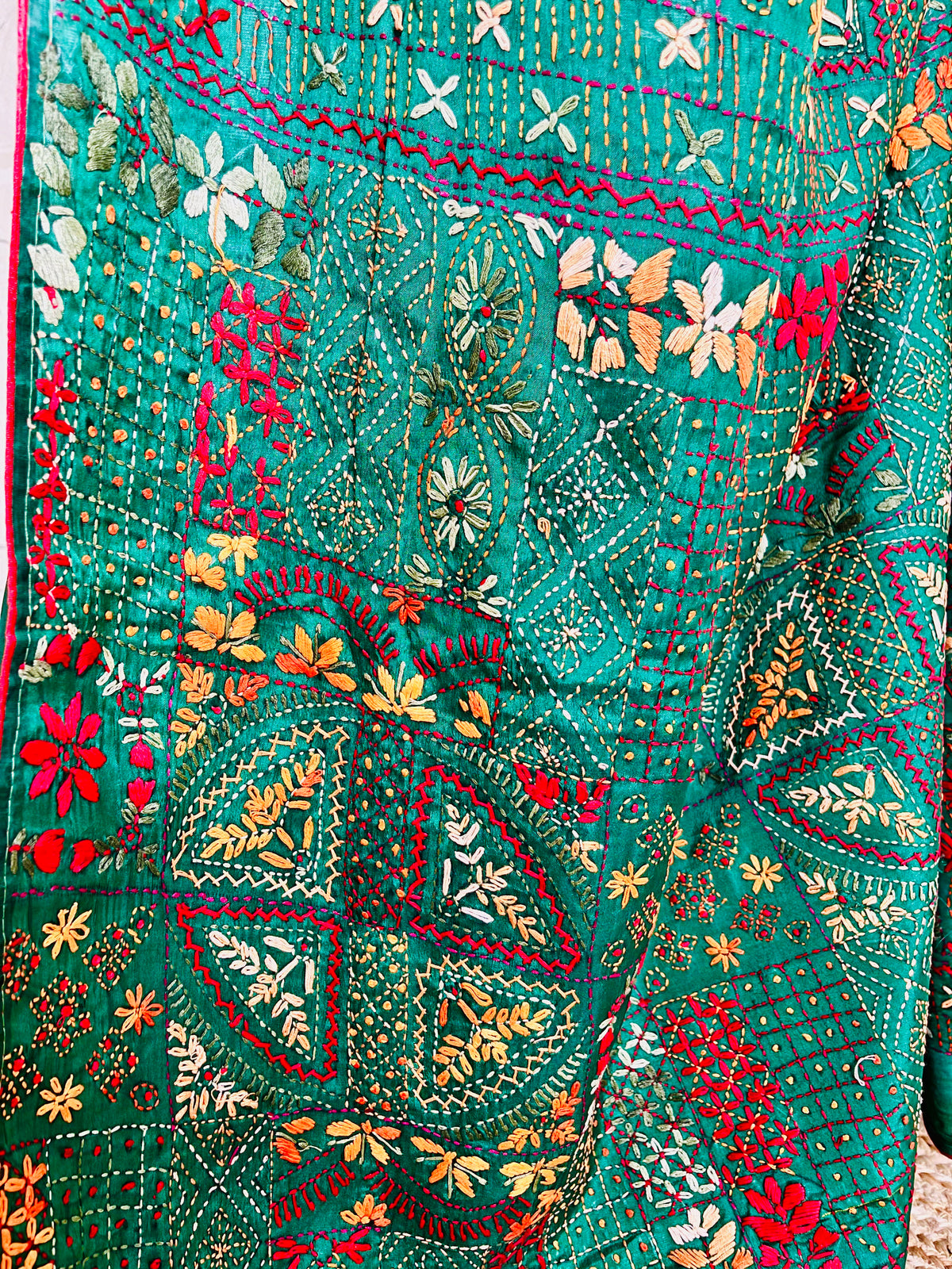 Close-up seated view of emerald green Lambani embroidered saree with red border